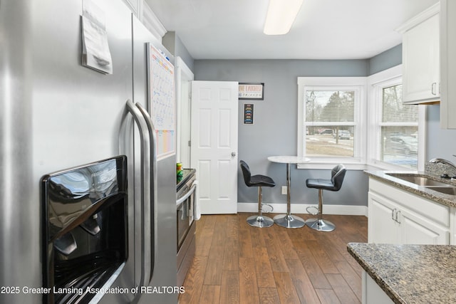 kitchen featuring baseboards, dark wood-style floors, appliances with stainless steel finishes, white cabinetry, and a sink