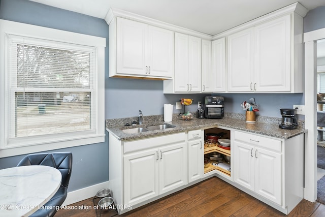 kitchen featuring light stone counters, dark wood-style flooring, white cabinetry, a sink, and baseboards