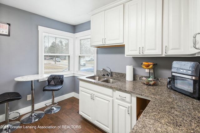 kitchen featuring dark wood-type flooring, white cabinets, a sink, dark stone countertops, and baseboards