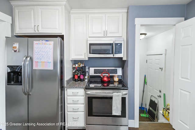 kitchen with appliances with stainless steel finishes, white cabinetry, dark stone countertops, and wood finished floors