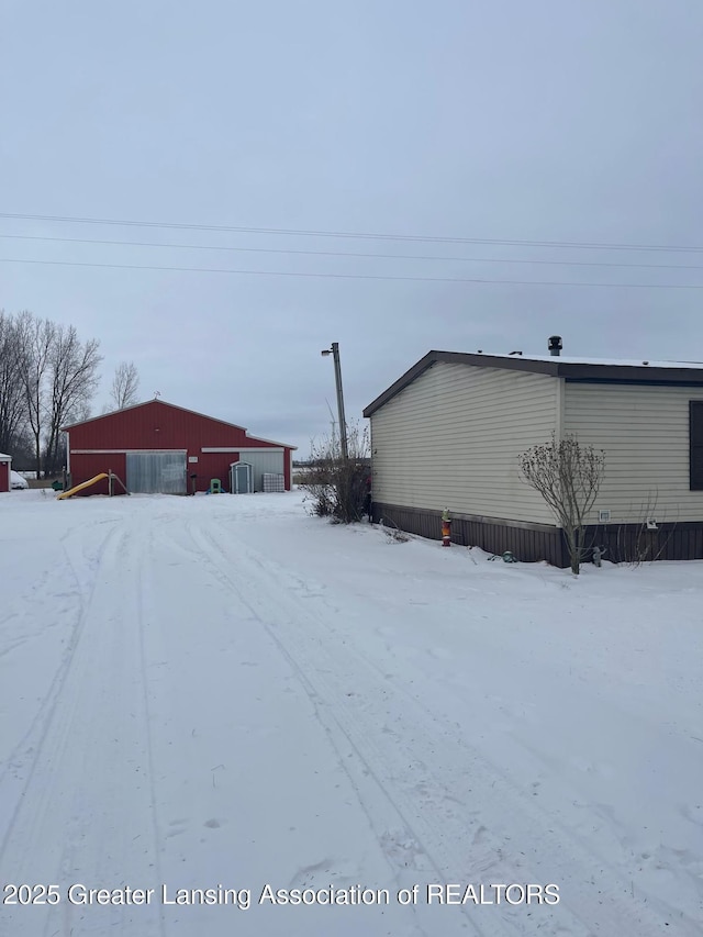 snowy yard with a detached garage, an outbuilding, and a pole building