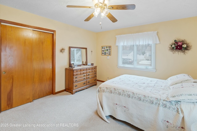 bedroom featuring light carpet, ceiling fan, baseboards, and a closet