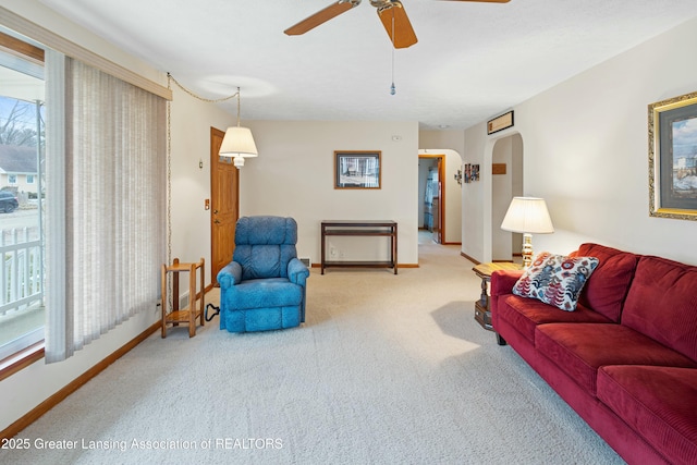 carpeted living area featuring a ceiling fan, arched walkways, and baseboards