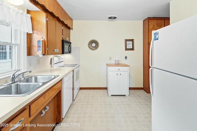 kitchen with brown cabinets, light countertops, visible vents, a sink, and white appliances