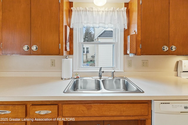 kitchen with brown cabinetry, white dishwasher, light countertops, and a sink