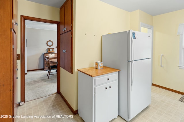 kitchen with freestanding refrigerator, light countertops, light carpet, and baseboards