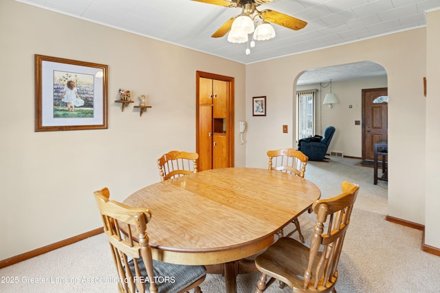 dining space featuring a ceiling fan, arched walkways, light carpet, and baseboards