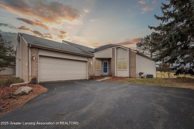 view of front of house with a garage, driveway, roof with shingles, cooling unit, and brick siding