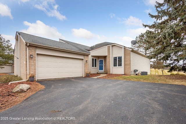 view of front of home featuring an attached garage, central air condition unit, brick siding, driveway, and roof with shingles