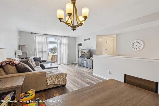 living room with an inviting chandelier, baseboards, visible vents, and wood finished floors