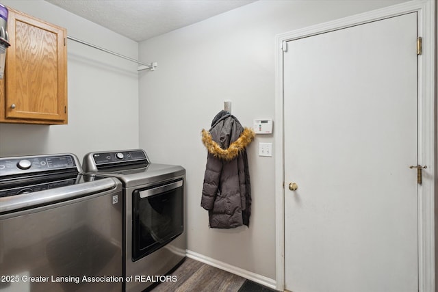 clothes washing area featuring a textured ceiling, dark wood-type flooring, baseboards, cabinet space, and washing machine and clothes dryer