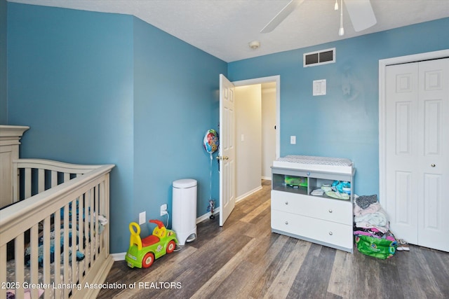 bedroom with visible vents, ceiling fan, wood finished floors, a nursery area, and baseboards