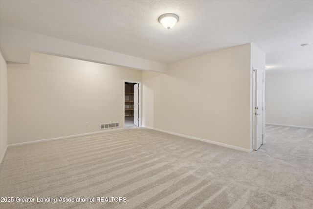 spare room with light colored carpet, visible vents, a textured ceiling, and baseboards