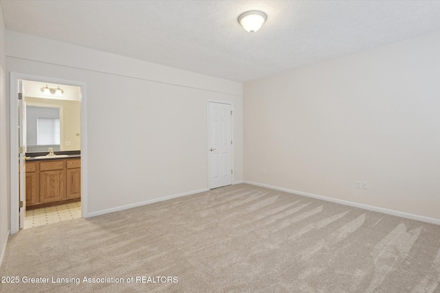 unfurnished bedroom featuring baseboards, ensuite bathroom, a sink, and light colored carpet