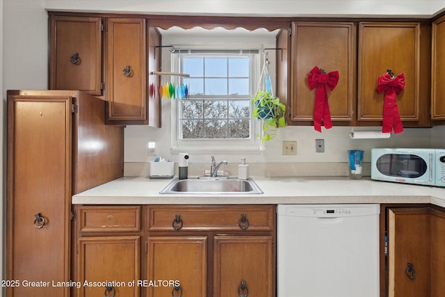 kitchen featuring white appliances, brown cabinets, a sink, and light countertops