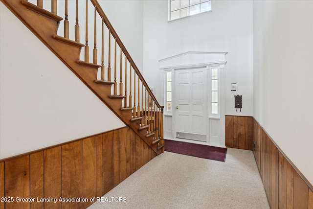 carpeted entryway with wooden walls, stairway, and wainscoting