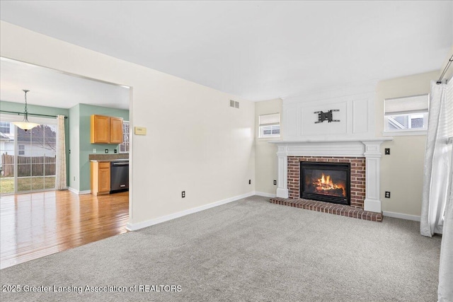 unfurnished living room featuring light carpet, a brick fireplace, and baseboards