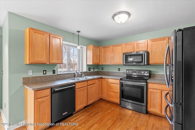 kitchen with appliances with stainless steel finishes, decorative light fixtures, light brown cabinetry, light wood-style floors, and a sink