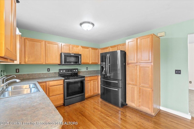 kitchen featuring light brown cabinetry, appliances with stainless steel finishes, a sink, and light wood-style flooring