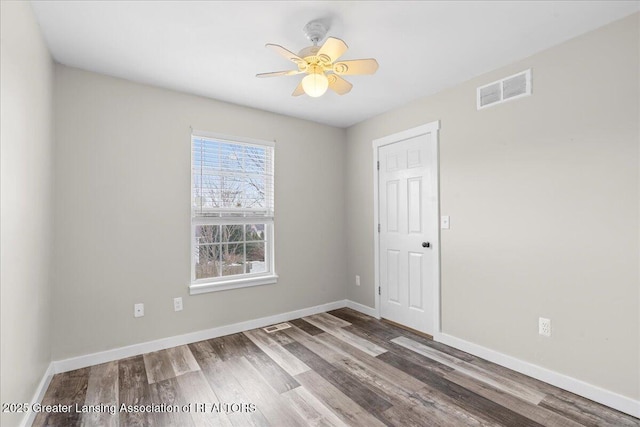 spare room featuring baseboards, visible vents, ceiling fan, and wood finished floors