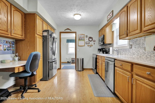 kitchen featuring light wood finished floors, brown cabinetry, appliances with stainless steel finishes, light countertops, and backsplash