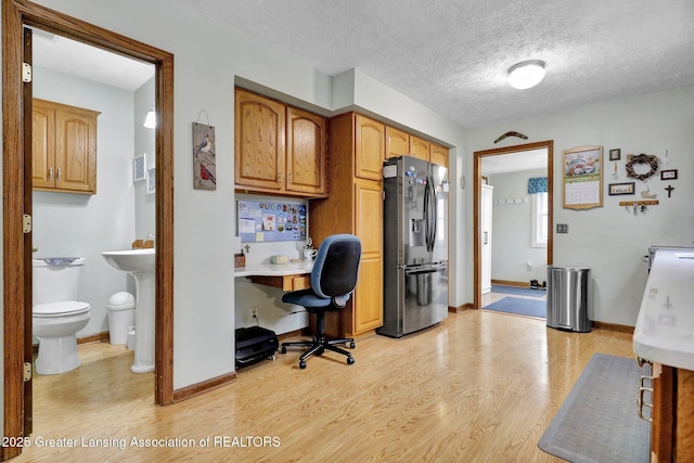 office featuring light wood-style flooring, a textured ceiling, baseboards, and built in desk