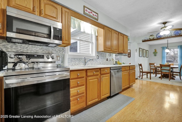 kitchen featuring brown cabinetry, stainless steel appliances, light countertops, light wood-type flooring, and a sink