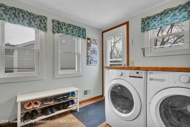 laundry area with washing machine and dryer, laundry area, wood finished floors, visible vents, and baseboards