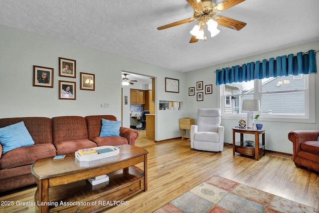 living area featuring a ceiling fan, baseboards, a textured ceiling, and light wood finished floors