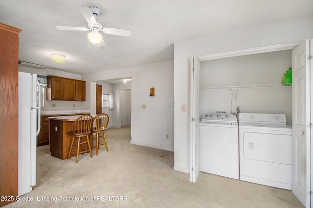 kitchen featuring a breakfast bar, light countertops, brown cabinetry, freestanding refrigerator, and independent washer and dryer