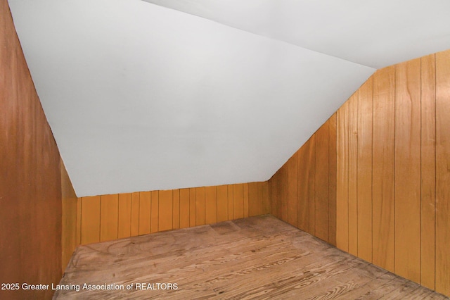 bonus room featuring vaulted ceiling, wooden walls, and wood finished floors