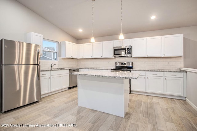 kitchen with light stone counters, vaulted ceiling, stainless steel appliances, white cabinetry, and a sink