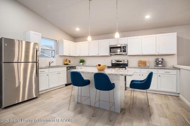 kitchen with backsplash, appliances with stainless steel finishes, white cabinets, vaulted ceiling, and a kitchen island