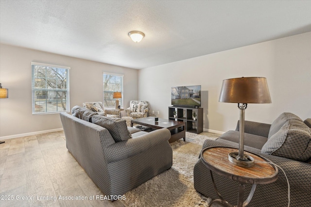 living room with a textured ceiling, light wood-style flooring, and baseboards