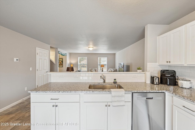 kitchen with tasteful backsplash, white cabinets, dishwasher, a peninsula, and a sink