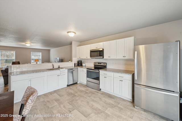 kitchen with appliances with stainless steel finishes, white cabinets, a peninsula, and decorative backsplash