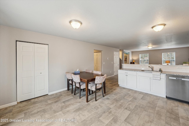 kitchen with dishwasher, light stone counters, light wood-style floors, white cabinetry, and a sink