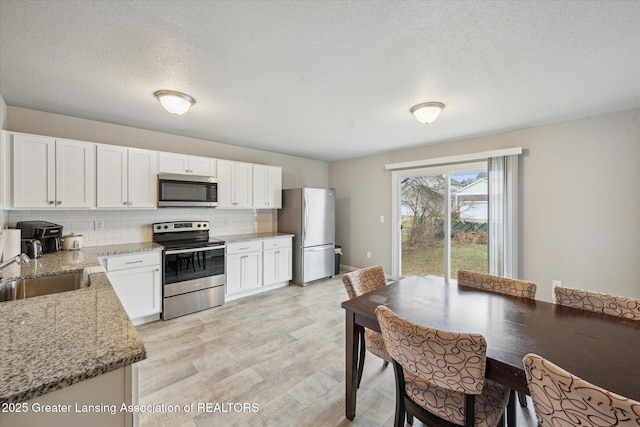 kitchen with light wood finished floors, stainless steel appliances, backsplash, white cabinets, and a sink