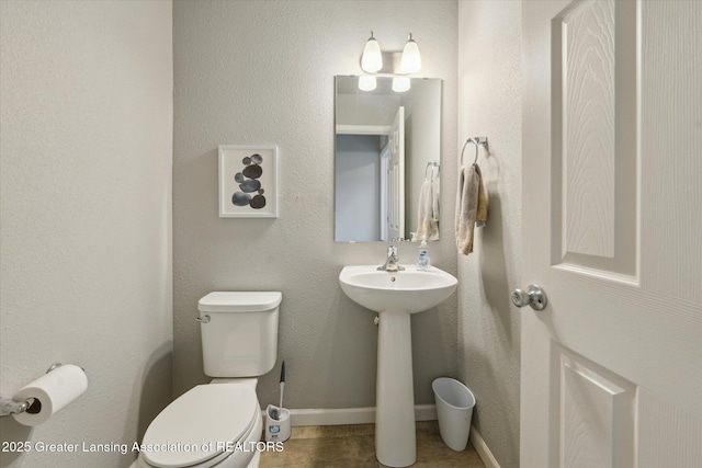 half bathroom featuring baseboards, a sink, toilet, and wood finished floors