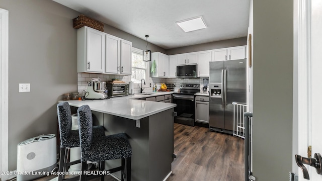 kitchen featuring stainless steel appliances, tasteful backsplash, a sink, a peninsula, and a kitchen breakfast bar