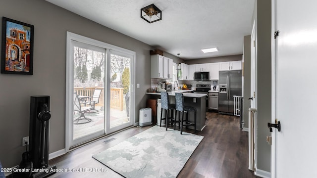 kitchen with a peninsula, white cabinetry, light countertops, stainless steel fridge, and a kitchen bar