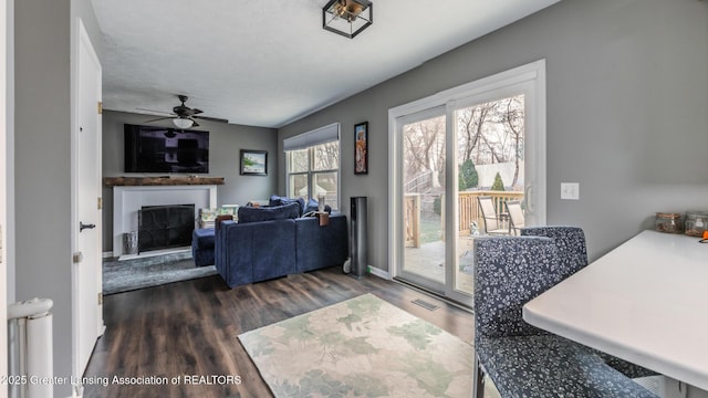 interior space with a fireplace, visible vents, a ceiling fan, baseboards, and dark wood finished floors