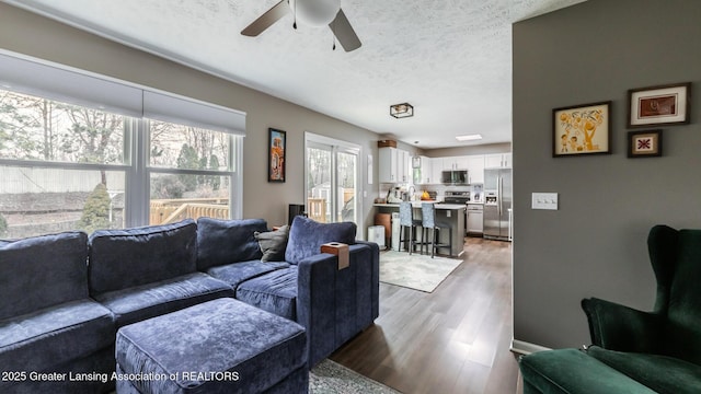 living room featuring light wood finished floors, ceiling fan, and a textured ceiling