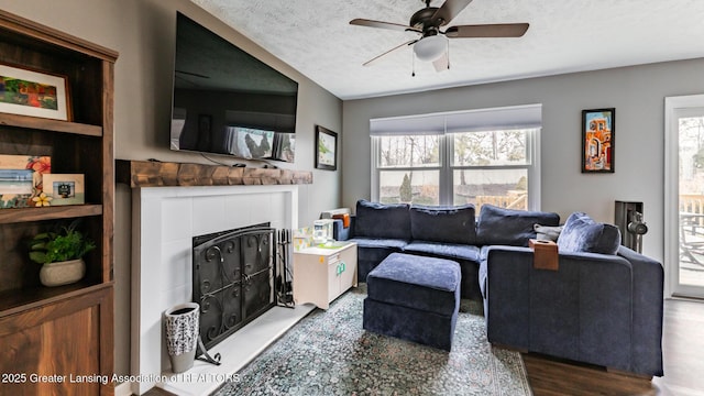 living room featuring a ceiling fan, a fireplace with raised hearth, a textured ceiling, and wood finished floors