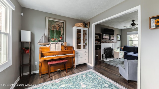 living area featuring a fireplace with flush hearth, a ceiling fan, a textured ceiling, wood finished floors, and baseboards