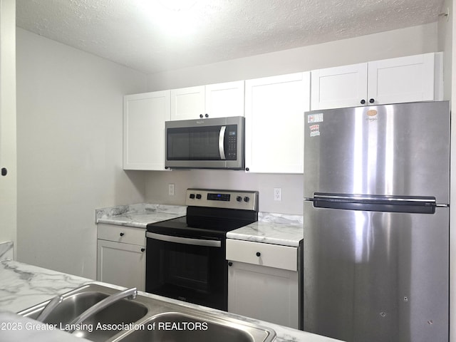 kitchen featuring light stone counters, stainless steel appliances, a textured ceiling, white cabinetry, and a sink