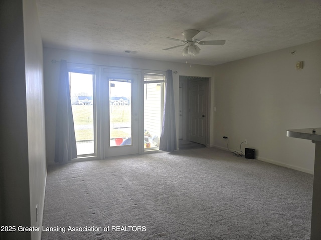 empty room featuring a textured ceiling, carpet flooring, visible vents, and a ceiling fan