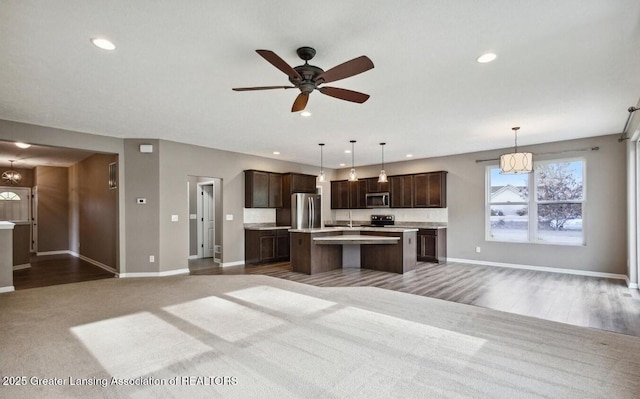 kitchen with stainless steel appliances, open floor plan, dark brown cabinets, light countertops, and a center island