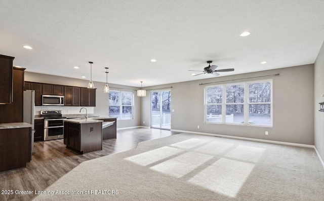 kitchen featuring stainless steel appliances, open floor plan, dark brown cabinets, light countertops, and a center island with sink