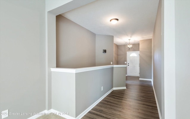 hall featuring a notable chandelier, baseboards, and dark wood-type flooring